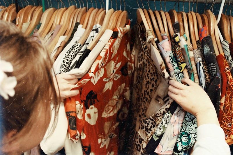 A young woman looking through a rail of colourful secondhand clothes on wooden hangers