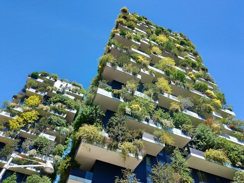 Milan's Bosco Verticale towers, their balconies filled with trees against a deep blue sky