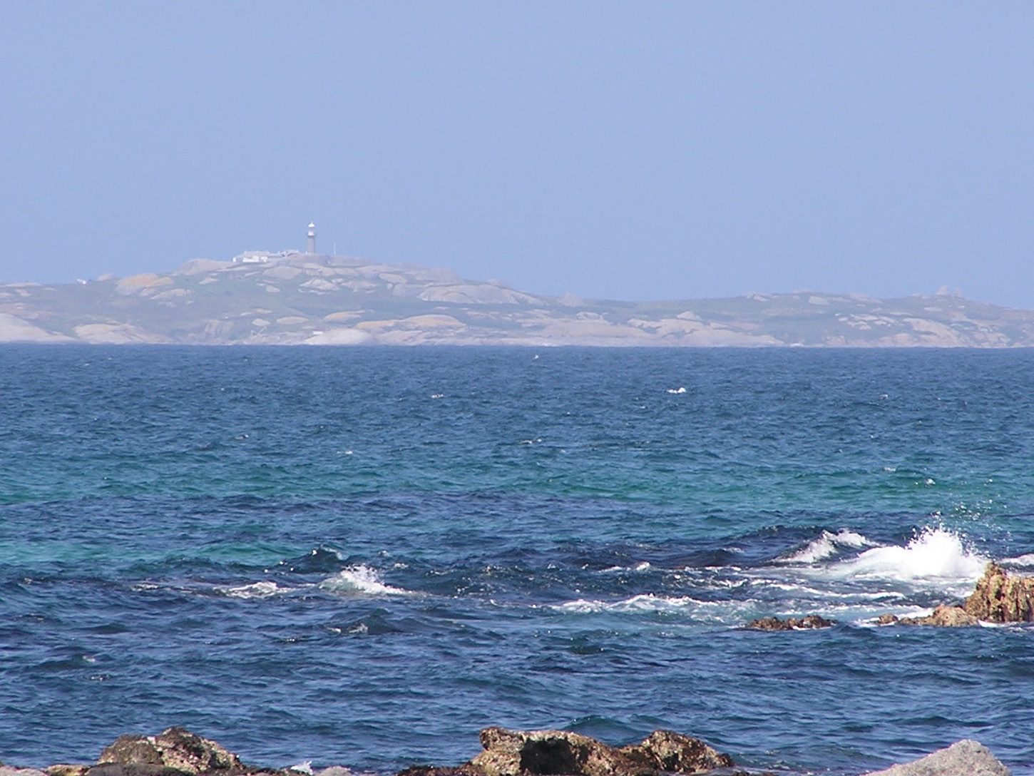 Barunguba Montague Island seen across deep blue water from the rocks at Narooma, the lighthouse small on its ridge