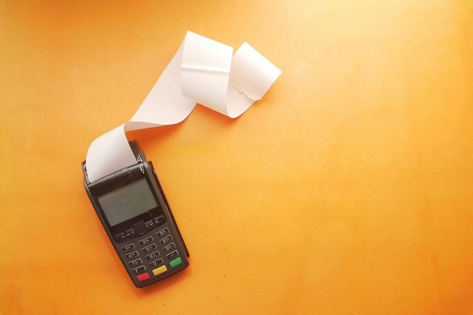 A payment terminal with a long paper receipt curling out, on a bright orange background