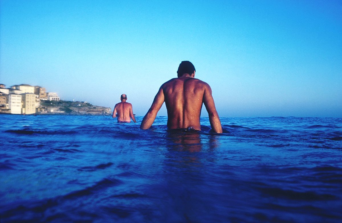 Two bathers wading into deep blue water at Bondi