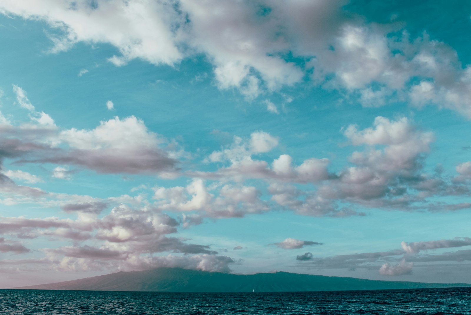 Soft white clouds drifting over a calm teal sea
