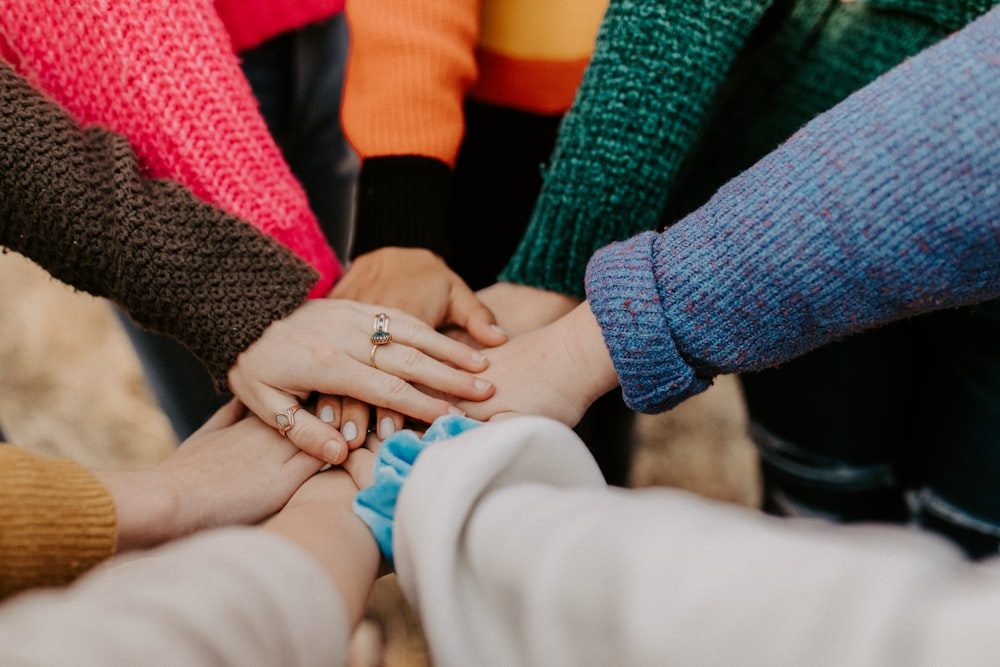 Several people in colourful jumpers placing their hands together in a circle