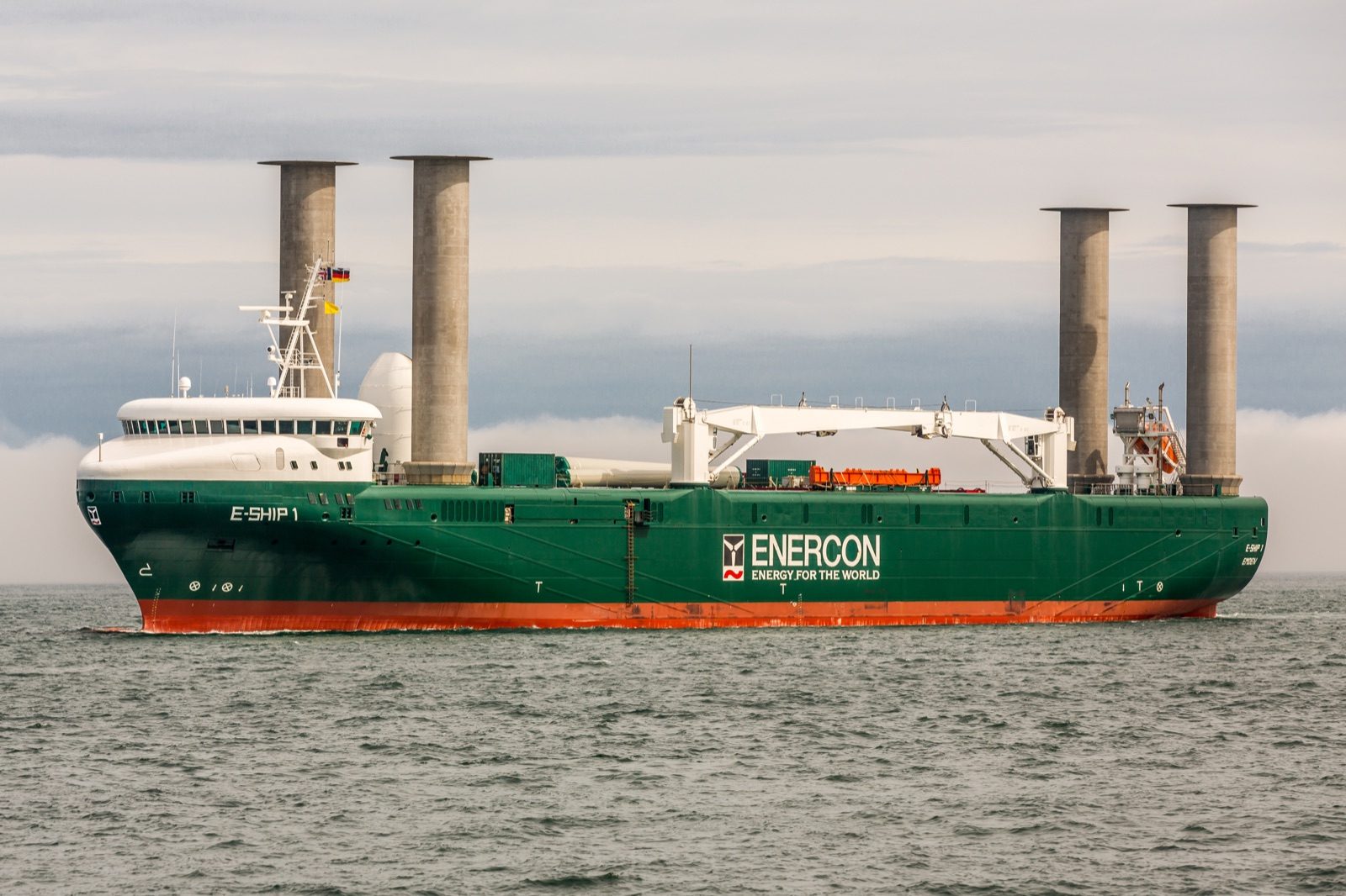E Ship 1, a green hulled cargo ship with four tall rotor sail cylinders on her deck, at sea